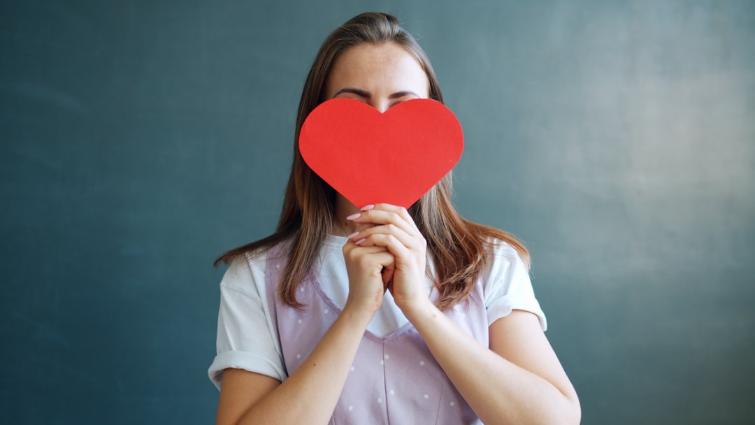 Woman holding a red heart in front of her face.